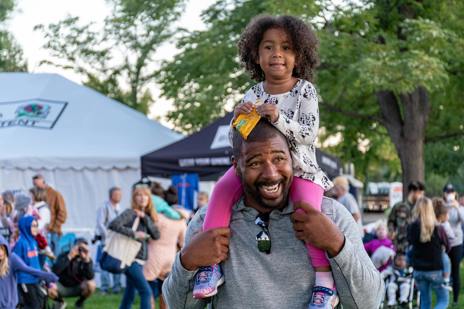 Girl sat on father's shoulders at an outdoor event, smiling