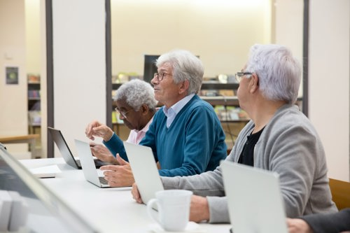 A line of older people sat at a desk with laptops
