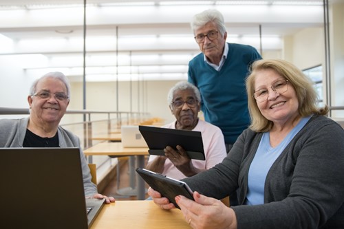 A group of elderly people at a table with a laptop and tablets